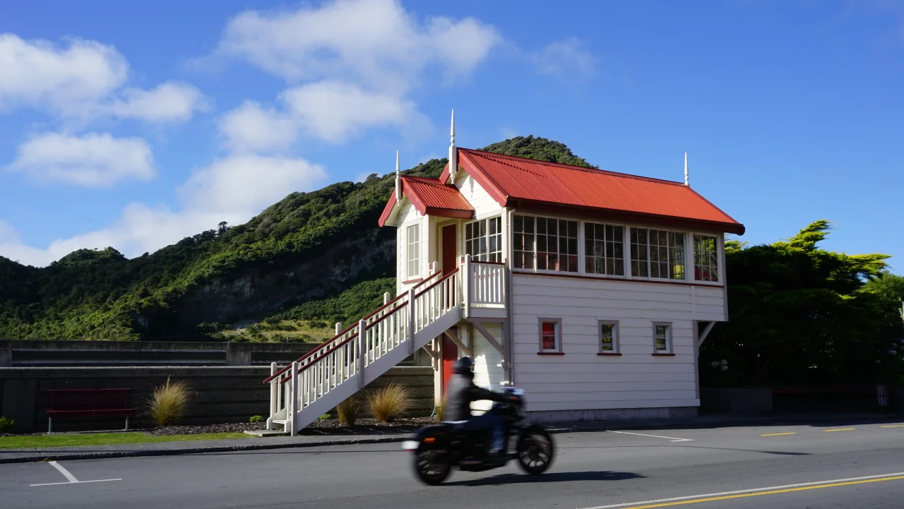 Historic heritage railway signal box with red roof beside green hills in Greymouth on the West Coast of New Zealand