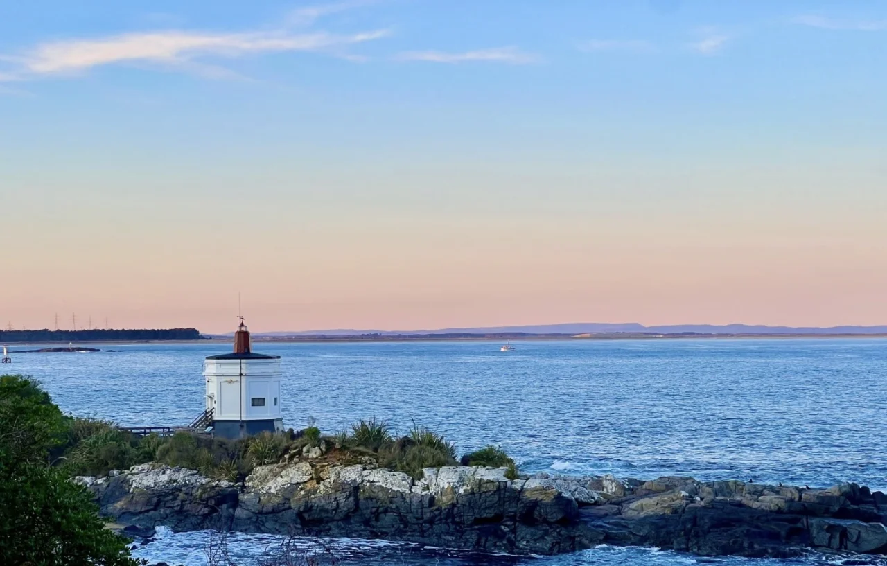 Historic white lighthouse on rocky headland at sunset overlooking Foveaux Strait near Invercargill Southland New Zealand